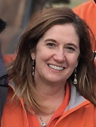 Smiling woman with brown hair wearing orange jacket.