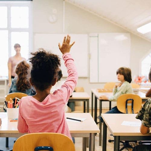 Children raising their hands in a classroom.