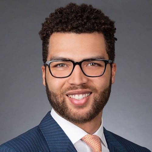 A man wearing glasses and a suit smiles for the camera.