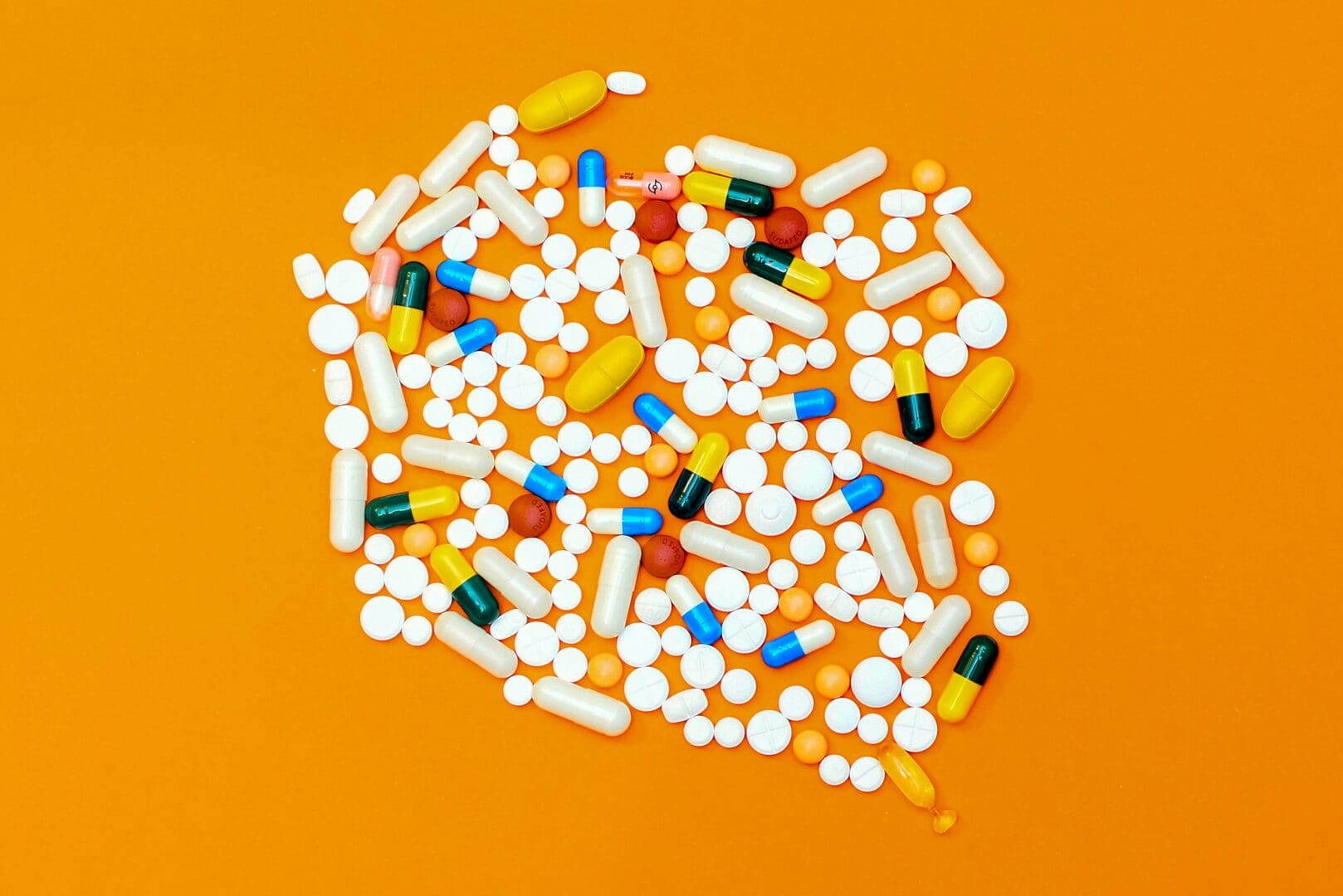 An assortment of colorful pills and capsules spread out on an orange background, representing various types of medication and pharmaceuticals.