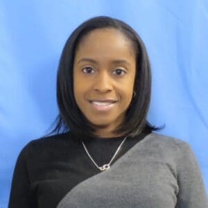 A woman with shoulder-length hair wearing a black top against a blue background.