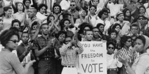 Black and white photo of a crowd of people with a sign that reads "You have the freedom to vote."