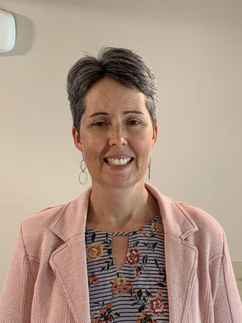 Smiling woman in pink blazer and floral shirt.