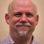 Smiling man with goatee wearing a button-down shirt.