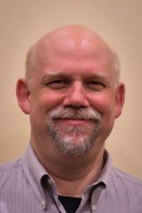 Smiling man with goatee wearing a button-down shirt.