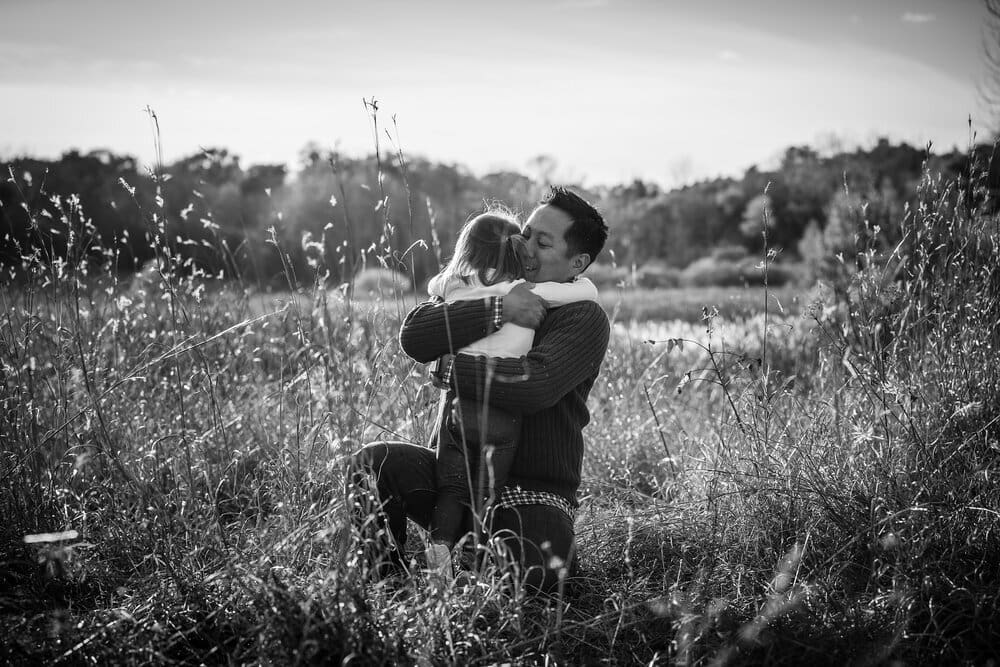 Man and daughter hug in a field.