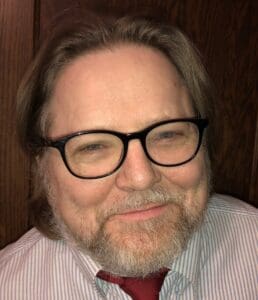 Man with glasses and a beard smiling.