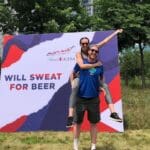 Couple posing in front of "Will Sweat For Beer" sign.