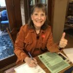 Woman wearing orange shirt gives thumbs up.