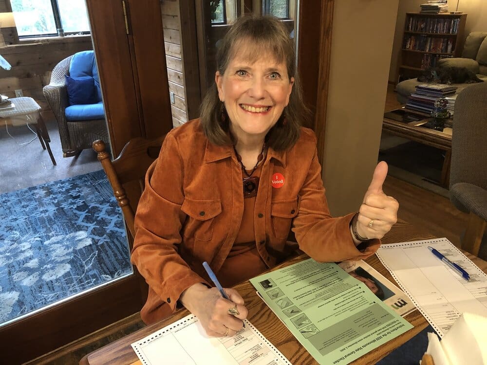 Woman wearing orange shirt gives thumbs up.