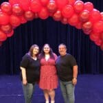 Three women smiling under a balloon arch.