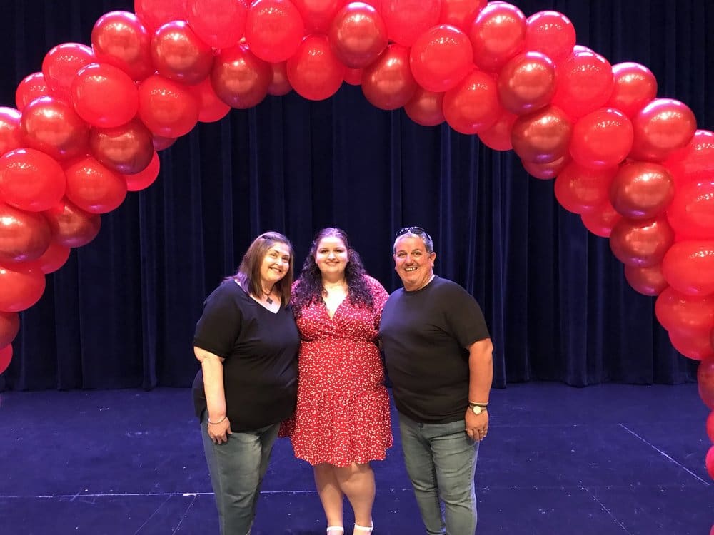 Three women smiling under a balloon arch.