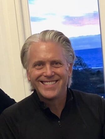 Smiling man with grey hair in black shirt.