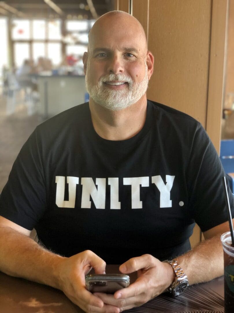 Man wearing a unity shirt, holding a phone.