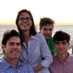 A family of four smiling by the ocean.