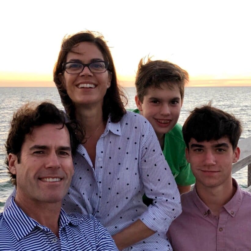 A family of four smiling by the ocean.