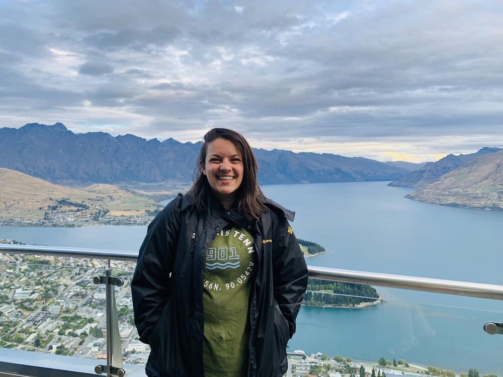 Woman smiling on a mountain overlooking a lake.