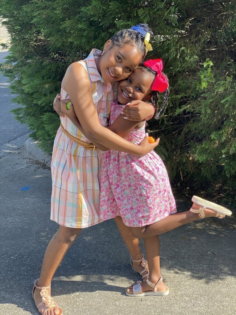 Two young girls hugging in dresses.