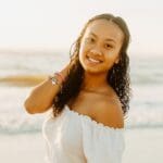 Smiling woman wearing a white top at the beach.