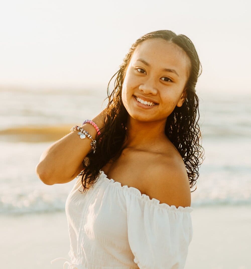 Smiling woman wearing a white top at the beach.