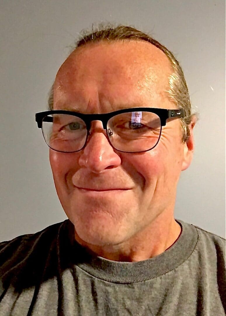 A man wearing glasses and a grey shirt.