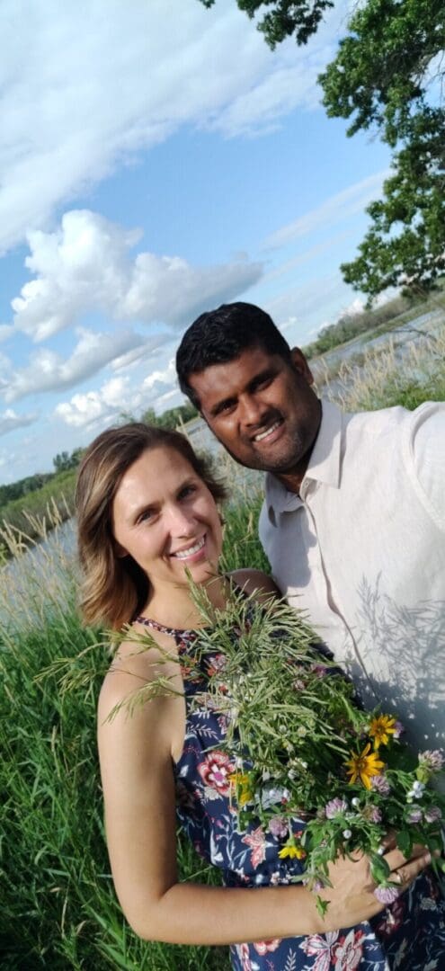 Couple smiling in a field with wildflowers.