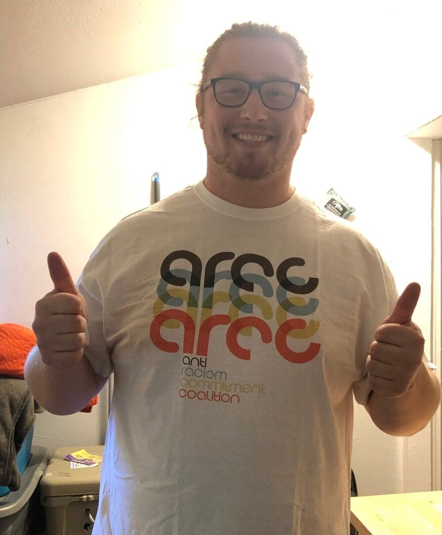 Man in white t-shirt with anti-racism logo.