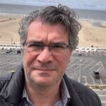 Man wearing glasses with beach in background.