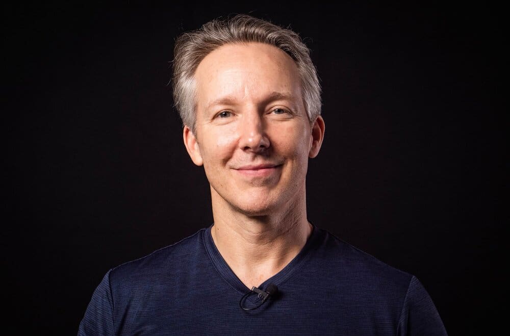 Smiling man in blue shirt against black background.