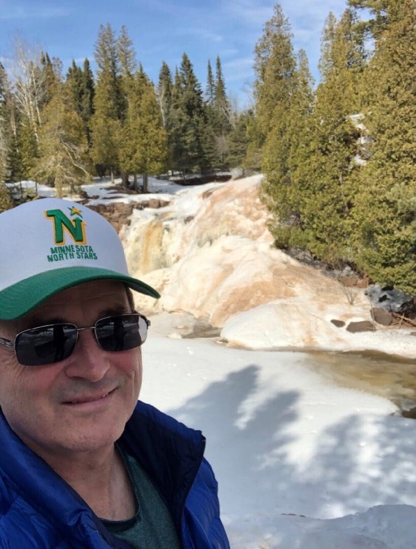 Man in sunglasses by a snowy waterfall.