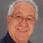 Smiling man wearing glasses and blue shirt.