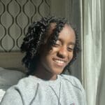 Smiling woman with curly hair wearing a grey sweatshirt.