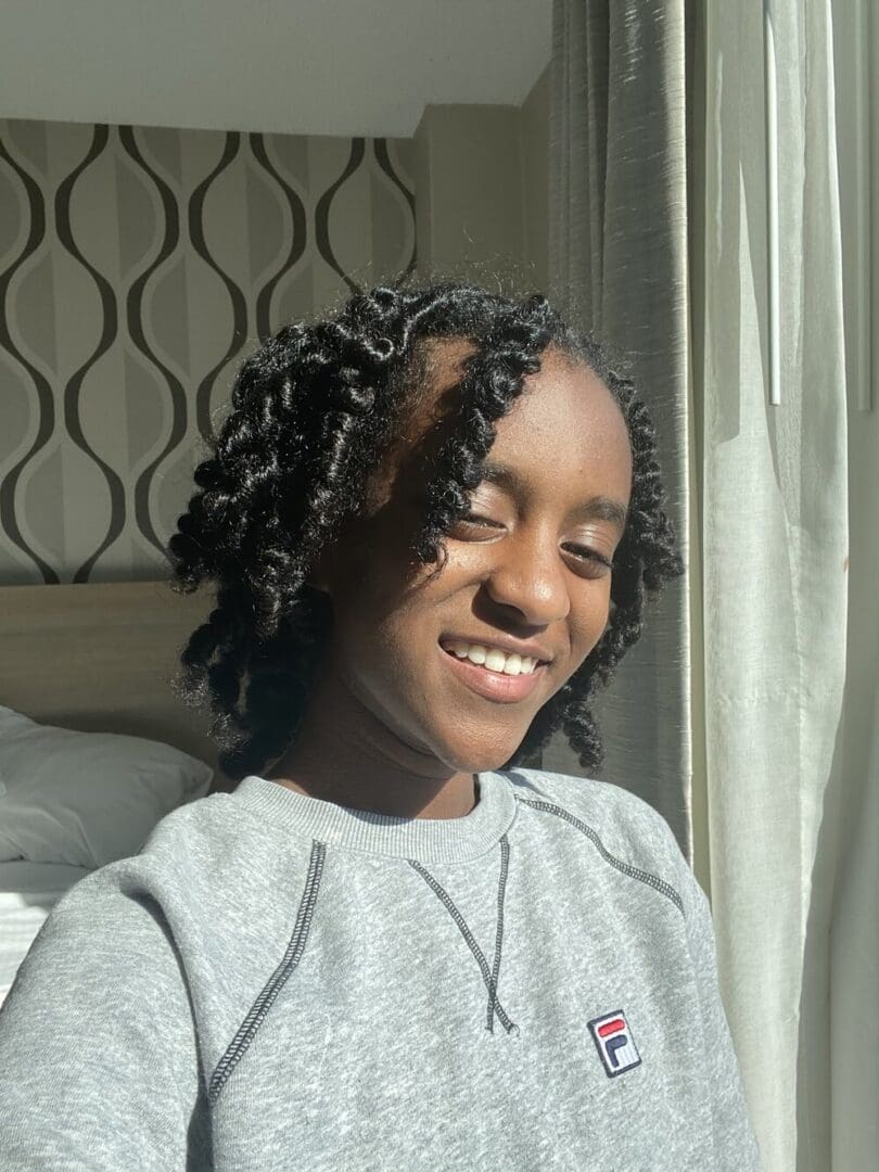 Smiling woman with curly hair wearing a grey sweatshirt.