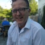 Smiling man wearing glasses and a white shirt.