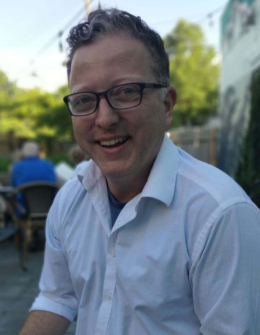 Smiling man wearing glasses and a white shirt.