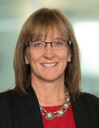 A woman with brown hair and glasses smiles.