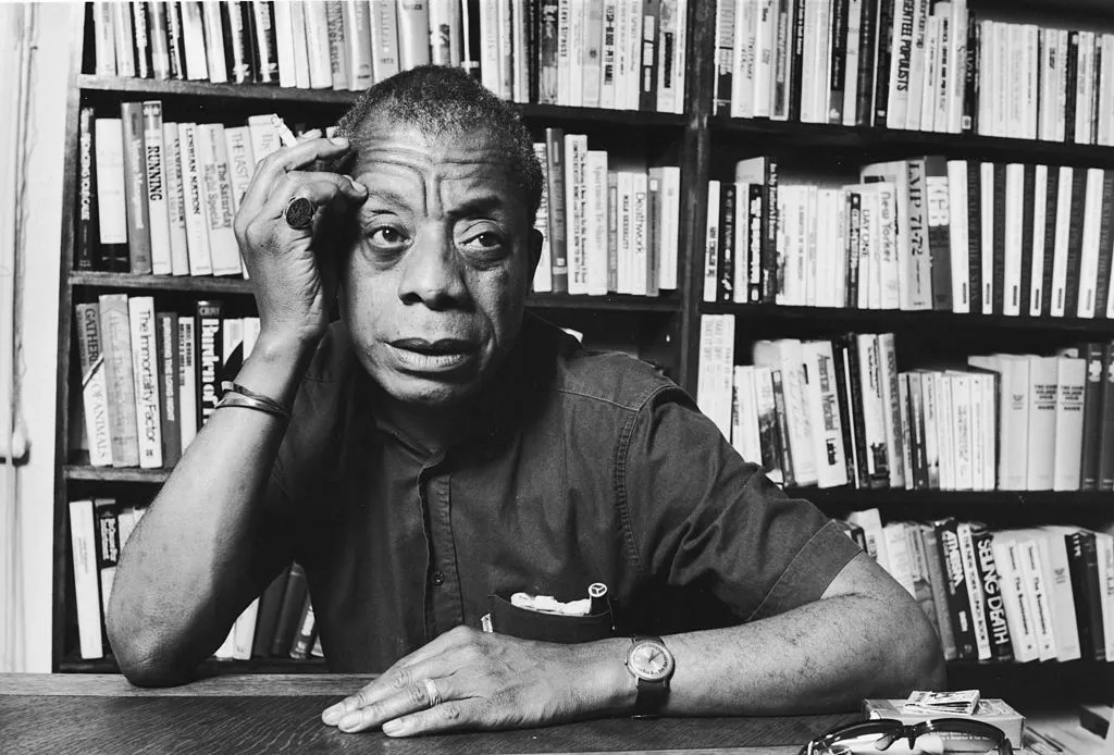 A black and white image of a man seated at a desk, surrounded by books, deep in thought or contemplation.