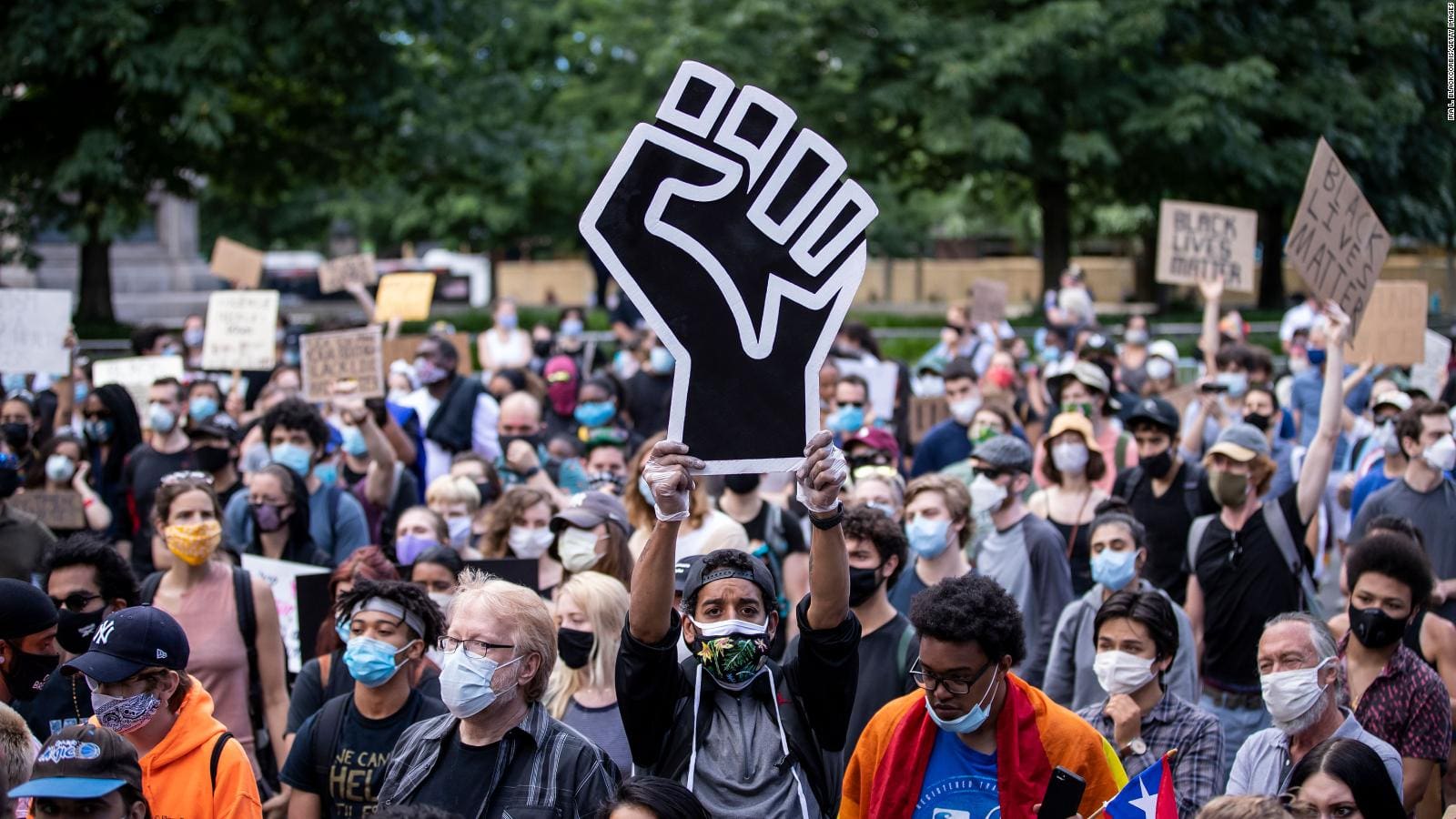 A gathering of people in masks, actively displaying signs to convey their thoughts and opinions during a protest.