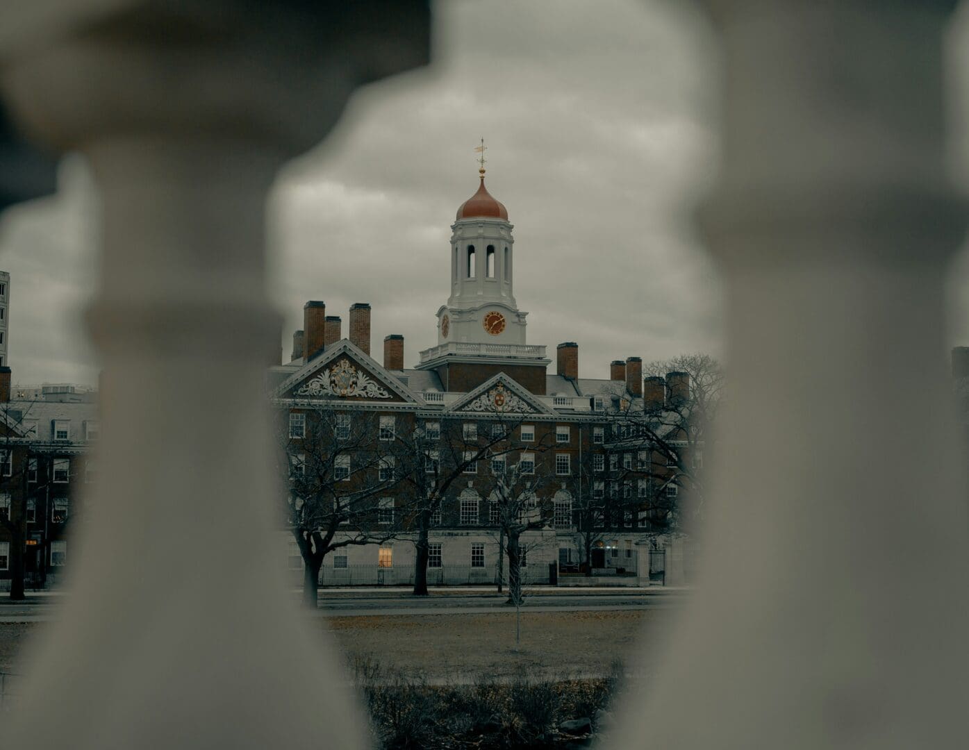 A view of a historic university building with a prominent clock tower and red dome, framed by architectural columns in the foreground, captured on a cloudy day.