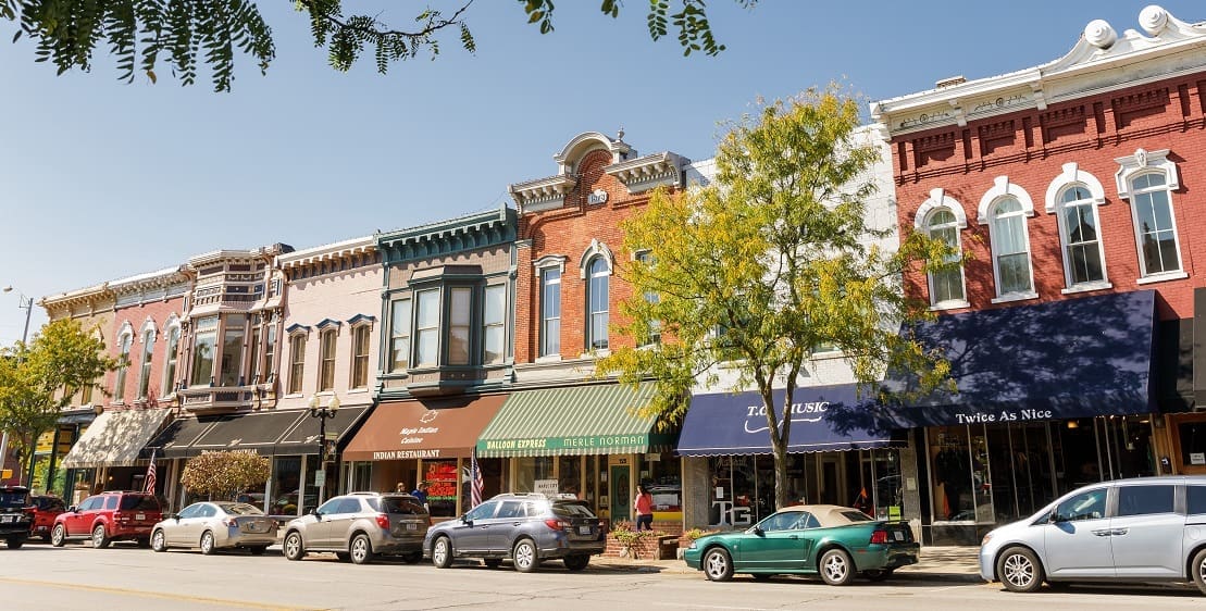 A bustling city street featuring a row of shops alongside parked cars, showcasing urban life and commerce