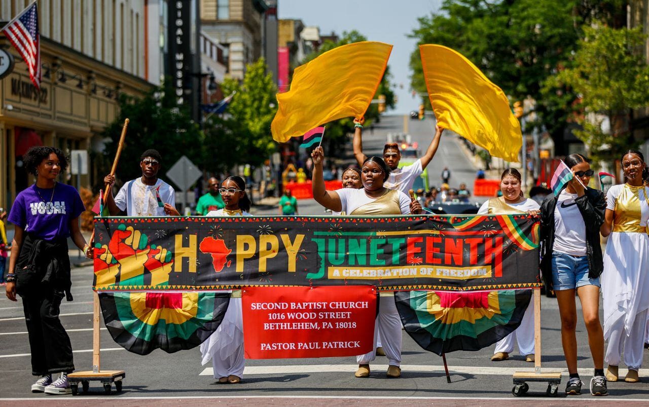 A diverse group of individuals in colorful costumes proudly displaying a banner at a festive event.