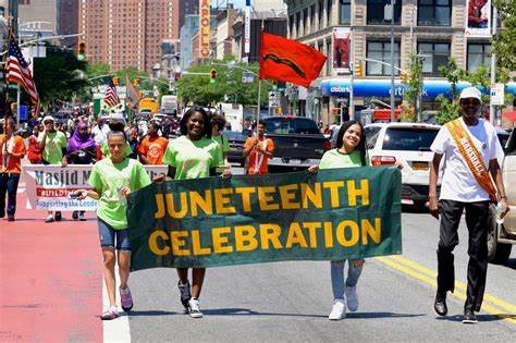 A diverse group of individuals walking together on the street, proudly displaying a banner for the Juneteenth celebration.