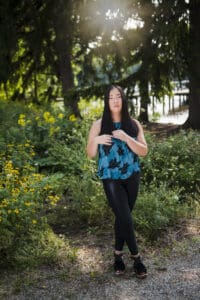 A woman wearing blue and black with trees in the back