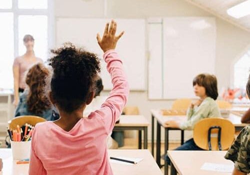 Children raising their hands in a classroom.