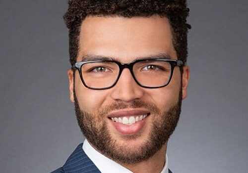 A man wearing glasses and a suit smiles for the camera.