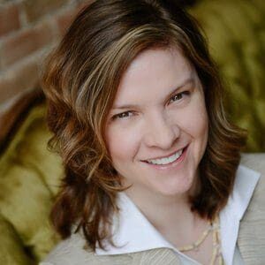 A woman smiling in front of a green couch.