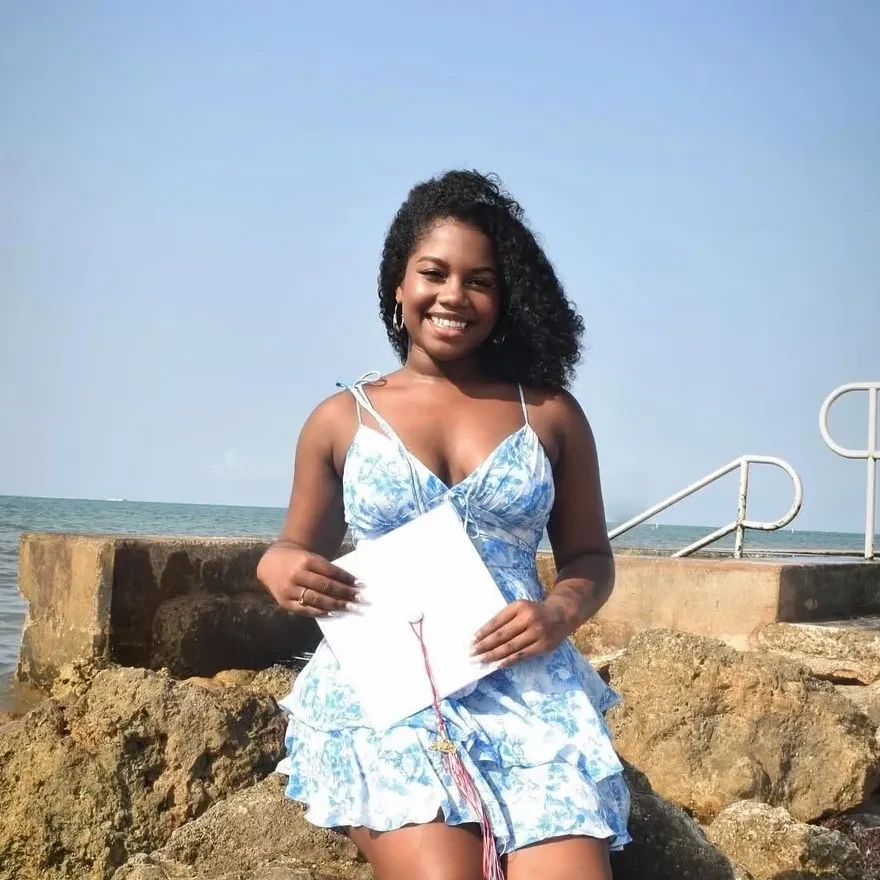 Woman smiling with certificate by the sea.