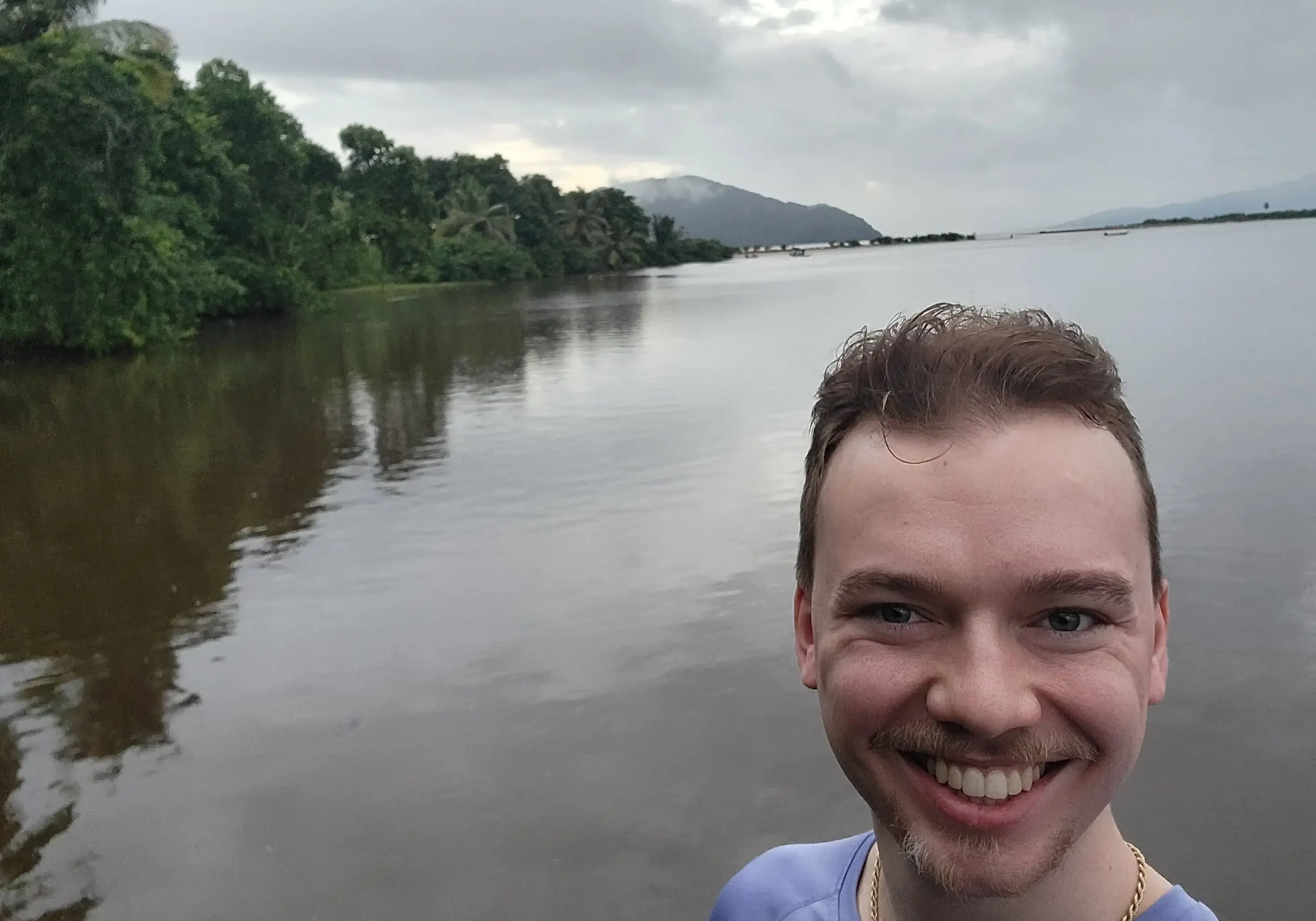 Smiling person near a calm riverside view.